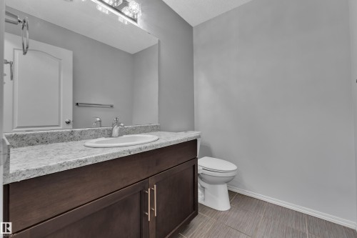 Bathroom vanity featuring a light-toned countertop, an undermount sink with a chrome faucet, and dark wood cabinetry with gold-tone hardware - 718 177 Street, Edmonton, AB - Indoor Photo Showing Bathroom
