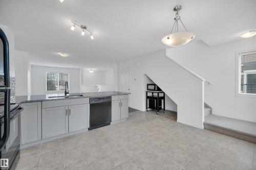Kitchen featuring a black granite countertop, light gray cabinetry, and a black dishwasher - 13 1030 Chappelle Boulevard, Edmonton, AB - Indoor Photo Showing Kitchen