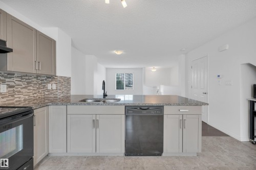 Kitchen with light gray cabinetry, a mosaic tile backsplash, and a dark stone-finish countertop - 13 1030 Chappelle Boulevard, Edmonton, AB - Indoor Photo Showing Kitchen With Double Sink