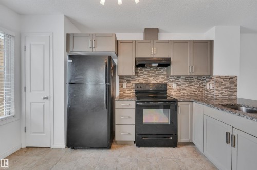 Kitchen featuring light gray cabinetry, dark granite-look countertops, a mosaic tile backsplash, black appliances, and neutral tile flooring - 13 1030 Chappelle Boulevard, Edmonton, AB - Indoor Photo Showing Kitchen