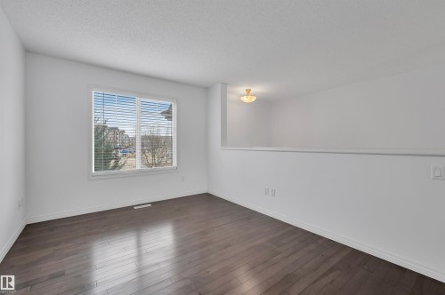 Spacious interior room with wood-finish flooring, white walls, and a large window with blinds - 13 1030 Chappelle Boulevard, Edmonton, AB - Indoor Photo Showing Other Room
