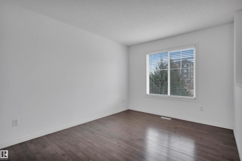 Spacious room featuring wood-finish flooring, white walls, and a large window with blinds - 13 1030 Chappelle Boulevard, Edmonton, AB - Indoor Photo Showing Other Room