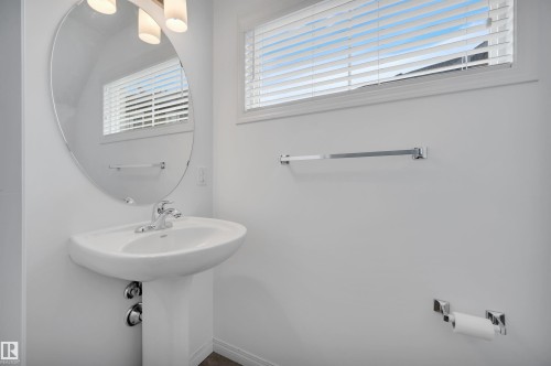 Pedestal sink with chrome faucet, complemented by an oval wall-mounted mirror and overhead vanity lighting - 13 1030 Chappelle Boulevard, Edmonton, AB - Indoor Photo Showing Bathroom