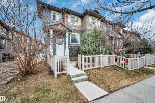 Multi-level townhouse exterior featuring a covered entry, white picket fencing, and a concrete walkway - 13 1030 Chappelle Boulevard, Edmonton, AB - Outdoor