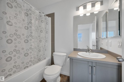 Bathroom featuring a white bathtub with tile surround, a toilet, and a vanity with an integrated sink - 13 1030 Chappelle Boulevard, Edmonton, AB - Indoor Photo Showing Bathroom