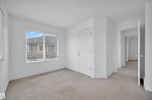 Bright room featuring two windows with blinds, light-colored carpeting, a paneled door, and neutral white wall finishes - 13 1030 Chappelle Boulevard, Edmonton, AB - Indoor Photo Showing Other Room