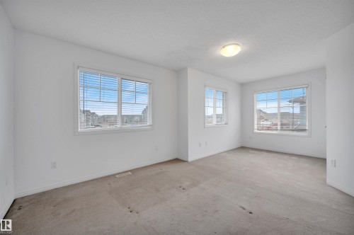 Spacious room featuring multiple windows with blinds, light-colored carpeting, white baseboards, and a flush-mount ceiling light fixture - 13 1030 Chappelle Boulevard, Edmonton, AB - Indoor Photo Showing Other Room