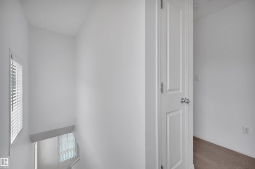 Staircase landing featuring white walls, a window with horizontal blinds, and a paneled interior door - 13 1030 Chappelle Boulevard, Edmonton, AB - Indoor Photo Showing Other Room
