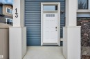 Front entry featuring a white paneled door with transom window, horizontal blue siding, architectural stone accents, and exterior lighting - 13 1030 Chappelle Boulevard, Edmonton, AB  - Outdoor With Exterior 