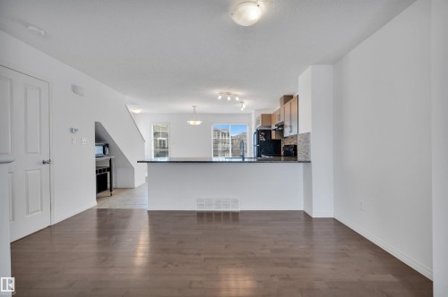 Spacious open-concept living area featuring wood-finish flooring, a kitchen island with a dark countertop, light wood cabinetry, and a mosaic tile backsplash - 13 1030 Chappelle Boulevard, Edmonton, AB - Indoor