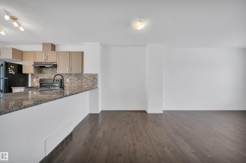Kitchen featuring a breakfast bar with stone countertop, tile backsplash, stainless steel appliances, and wood-finish flooring - 13 1030 Chappelle Boulevard, Edmonton, AB - Indoor Photo Showing Kitchen