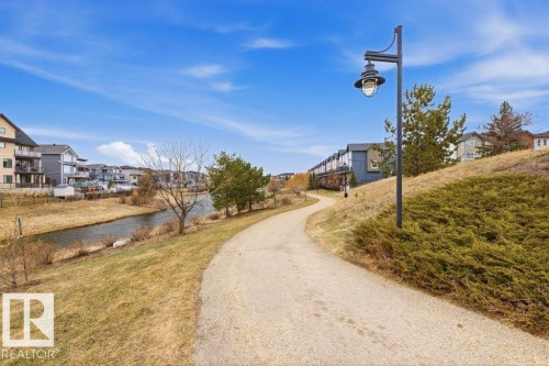 Paved pathway paralleling a natural waterway, bordered by grassy slopes and scattered trees - 18, 2560 Pegasus Boulevard, Edmonton, AB - Outdoor