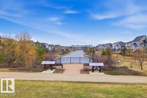 Community green space featuring a paved pathway, a pedestrian bridge over a waterway, and surrounding residential properties - 18, 2560 Pegasus Boulevard, Edmonton, AB - Outdoor With View