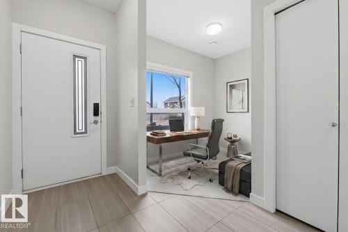 Entryway featuring wood-finish tile flooring, a contemporary white entrance door with vertical glass insert, and a recessed office space with a large window - 18, 2560 Pegasus Boulevard, Edmonton, AB - Indoor Photo Showing Office