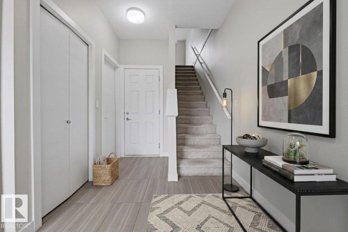 Entryway featuring wood-finish flooring, two panel doors, a carpeted staircase with white railing, and an overhead light fixture - 18, 2560 Pegasus Boulevard, Edmonton, AB - Indoor Photo Showing Other Room