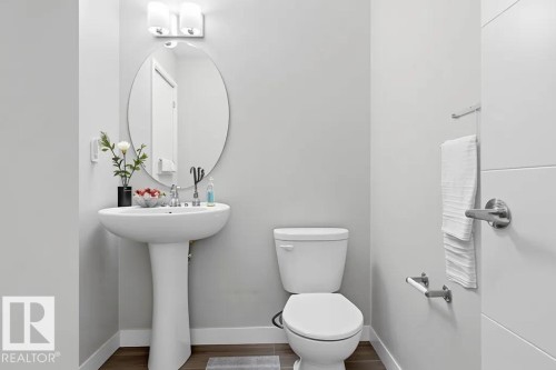 Bathroom featuring a white pedestal sink, oval mirror, and contemporary two-light vanity fixture - 18, 2560 Pegasus Boulevard, Edmonton, AB - Indoor Photo Showing Bathroom