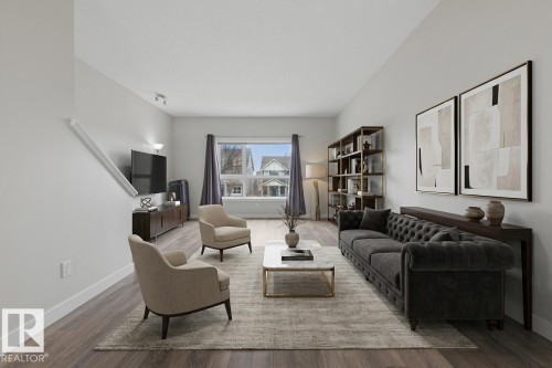 Spacious living area featuring wood-finish flooring, light grey wall paint, and a large window - 18, 2560 Pegasus Boulevard, Edmonton, AB - Indoor Photo Showing Living Room