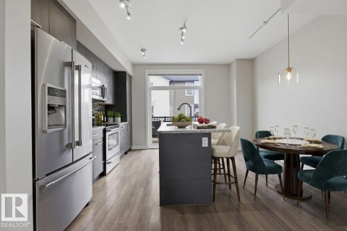 Contemporary kitchen and dining area featuring stainless steel appliances, dark cabinetry, and wood-finish flooring - 18, 2560 Pegasus Boulevard, Edmonton, AB - Indoor