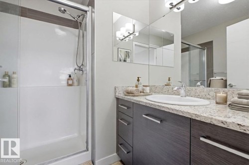Bathroom featuring a walk-in shower with clear glass enclosure, a single vanity with an integrated sink, a light-toned stone-finish countertop, and dark wood-finish cabinetry with silver-tone hardware - 18, 2560 Pegasus Boulevard, Edmonton, AB - Indoor Photo Showing Bathroom
