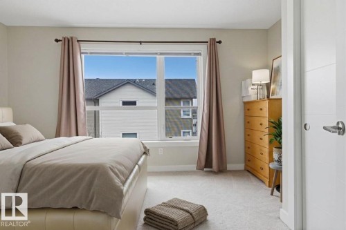 Bright bedroom featuring a large window, neutral carpeting, and a contemporary white door with horizontal paneling - 18, 2560 Pegasus Boulevard, Edmonton, AB - Indoor Photo Showing Bedroom