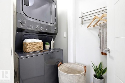 Dedicated laundry area featuring a stacked washer and dryer unit, wall-mounted drying rack, and modern white door - 18, 2560 Pegasus Boulevard, Edmonton, AB - Indoor Photo Showing Laundry Room