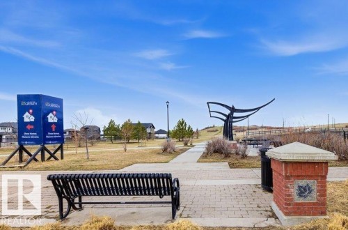 Community park space featuring a paved walkway, mature trees, a decorative metal sculpture, and a permanent park bench - 18, 2560 Pegasus Boulevard, Edmonton, AB - Outdoor