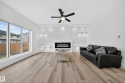 Spacious living area featuring light wood-finish flooring, a contemporary electric fireplace, and built-in illuminated shelving - 