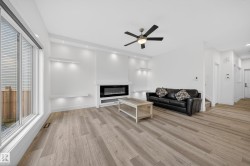 Spacious living area featuring light wood-finish flooring, a contemporary electric fireplace, and recessed wall lighting - 