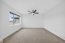 Spacious room featuring neutral carpet flooring, white walls, and a modern ceiling fan with integrated lighting - 