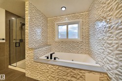 Soaking tub with matte black fixtures, surrounded by textured geometric wall tile and a window - 