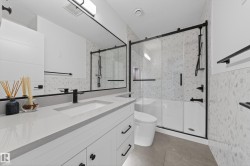 Contemporary bathroom featuring a spacious vanity with an integrated sink and light grey countertop, matte black fixtures, a large frameless mirror, and a shower-tub combination with sliding glass doors - 