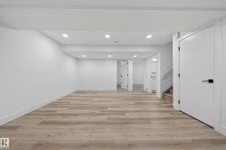 Spacious lower-level room featuring wood-finish flooring, recessed lighting, white walls, and contemporary doors with matte black hardware - 
