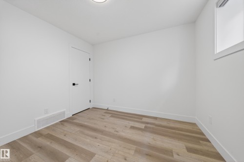 Room featuring wood-finish flooring, white walls, white trim, a white door with black hardware, and a single window - 7414 Chivers Crescent Sw, Edmonton, AB - Indoor Photo Showing Other Room