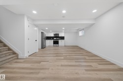 Open-concept lower level featuring recessed lighting, wood-finish flooring, a full kitchen with stainless steel appliances, and a window providing natural light - 