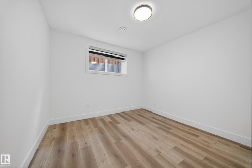 Room featuring wood-finish flooring, white walls, and a recessed window with horizontal blinds - 7414 Chivers Crescent Sw, Edmonton, AB - Indoor Photo Showing Other Room