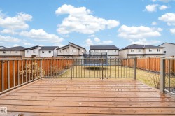 Expansive wood deck with metal railings overlooking a backyard with a grass lawn and wood fencing - 