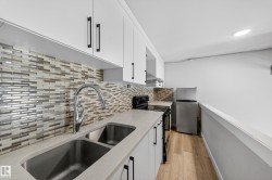 Contemporary kitchen featuring white cabinetry with black hardware, a stainless steel double basin sink, a pull-down faucet, and light wood-finish flooring - 