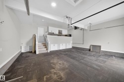 Spacious garage featuring dark wood-finish flooring, overhead lighting, and an integrated kitchenette with white cabinetry, a stone-look backsplash, and a built-in microwave - 