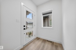 Entryway featuring a white door with three vertical glass panels, black hardware, and wood-finish flooring - 