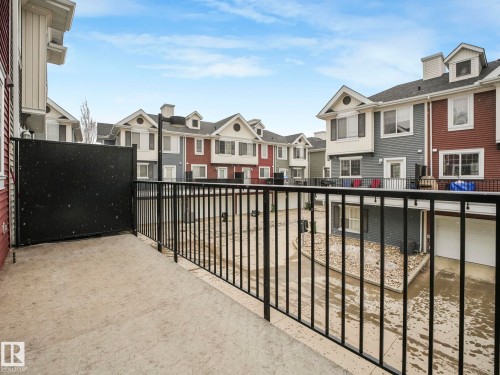 Private concrete balcony with black metal railings and a privacy screen, overlooking a multi-unit residential community featuring varied exterior siding and garage access - 96 8315 180 Avenue, Edmonton, AB - Outdoor With Balcony