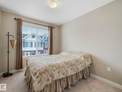 Room featuring a large window with white blinds and drapes, light neutral wall paint, and beige carpeting - 96 8315 180 Avenue, Edmonton, AB - Indoor Photo Showing Bedroom