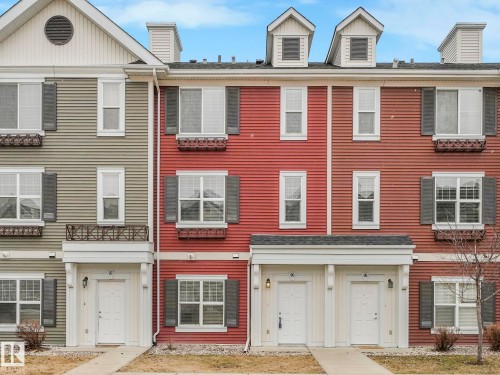 Multi-level townhome exterior featuring dormer windows, decorative window boxes, dark shutters, and a covered entry - 96 8315 180 Avenue, Edmonton, AB - Outdoor With Facade