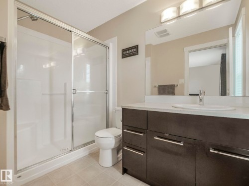Bathroom featuring a white shower with glass sliding doors, a dark wood-finish vanity with a light-colored countertop, and a rectangular mirror - 96 8315 180 Avenue, Edmonton, AB - Indoor Photo Showing Bathroom