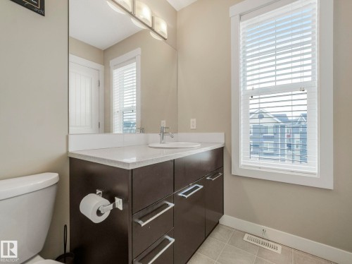 Contemporary bathroom featuring a dark wood-finish vanity with a white countertop and undermount sink, chrome faucet, and rectangular mirror - 96 8315 180 Avenue, Edmonton, AB - Indoor Photo Showing Bathroom