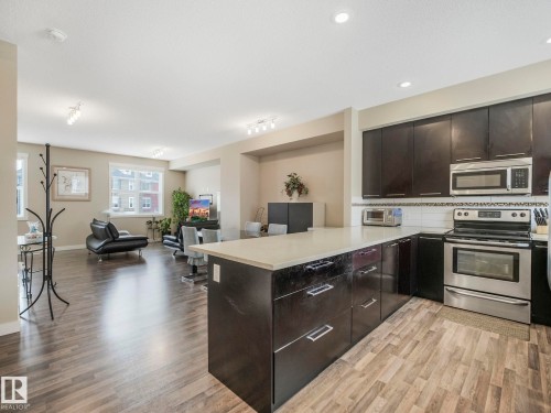 Open-concept kitchen featuring dark cabinetry, stainless steel appliances, and wood-finish flooring - 96 8315 180 Avenue, Edmonton, AB - Indoor Photo Showing Kitchen With Stainless Steel Kitchen With Upgraded Kitchen
