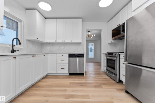 Modern kitchen featuring bright white cabinetry, a solid surface countertop with integrated backsplash, stainless steel appliances, a matte black faucet, and wood-finish flooring - 3208 130 Avenue, Edmonton, AB - Indoor Photo Showing Kitchen