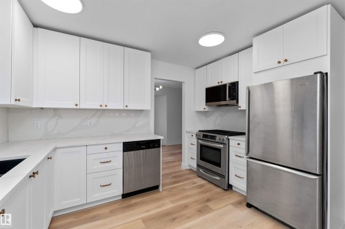 Kitchen featuring bright white cabinetry, stainless steel appliances, light wood-finish flooring, and white countertops with a matching backsplash - 3208 130 Avenue, Edmonton, AB - Indoor Photo Showing Kitchen