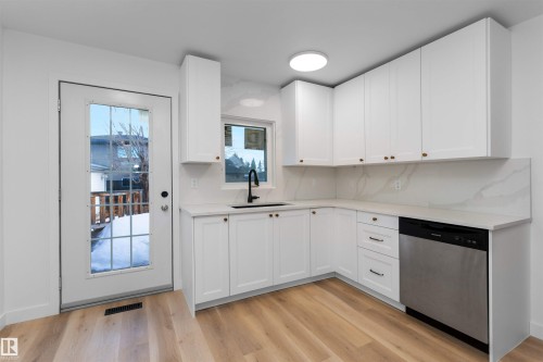 Modern kitchen featuring white shaker cabinetry, light wood-finish flooring, white countertops with integrated backsplash, a black gooseneck faucet, and a built-in stainless steel dishwasher - 3208 130 Avenue, Edmonton, AB - Indoor Photo Showing Kitchen