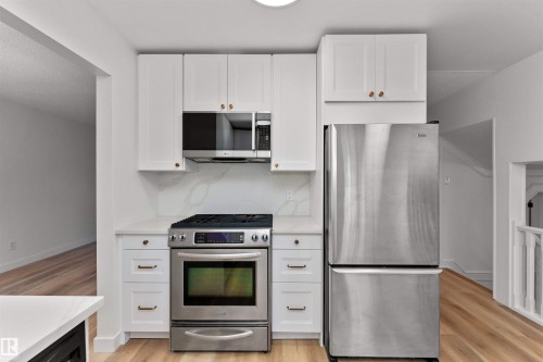 Modern kitchen featuring white cabinetry, stainless steel appliances, light-toned wood-finish flooring, and a stone-finish countertop with a matching backsplash - 3208 130 Avenue, Edmonton, AB - Indoor Photo Showing Kitchen