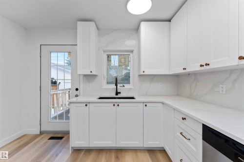 Contemporary kitchen featuring white cabinetry, light-toned wood-finish flooring, and solid surface countertops with a matching backsplash - 3208 130 Avenue, Edmonton, AB - Indoor Photo Showing Kitchen